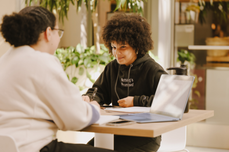 two students sit at a table studying and smiling.