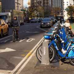 Citibikes lining New york city street as a cab and biker drive by