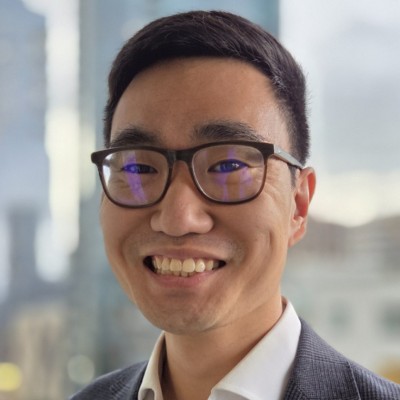A man wearing glasses standing in front of skyscrapers.