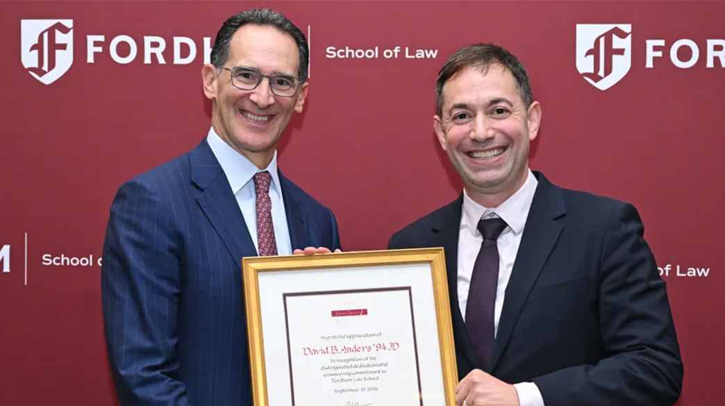Two men wearing suits holding a framed award.