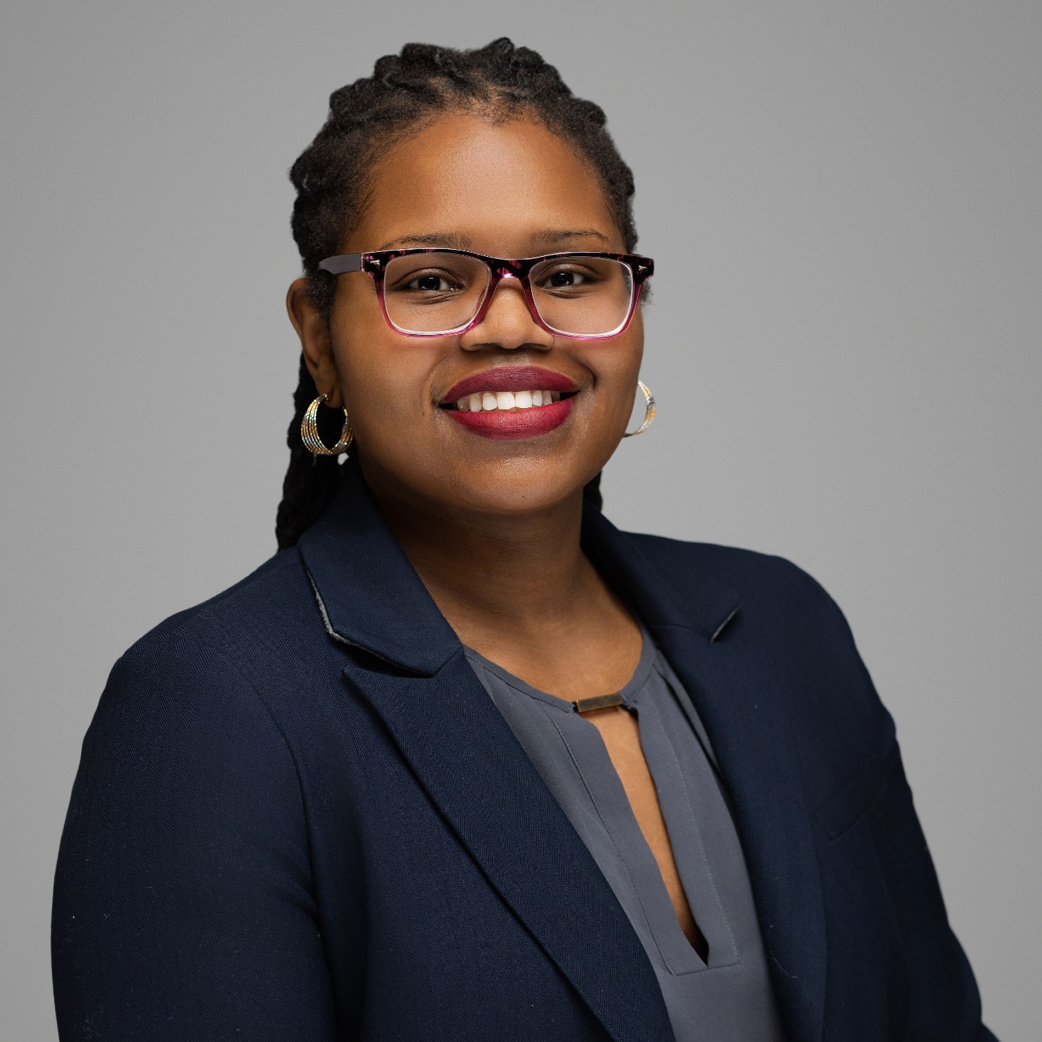 A woman wearing glasses and a dark blazer.