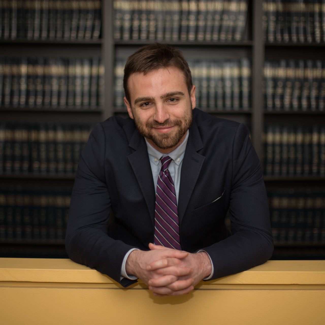 A man standing with his hands folded in front of bookcases.
