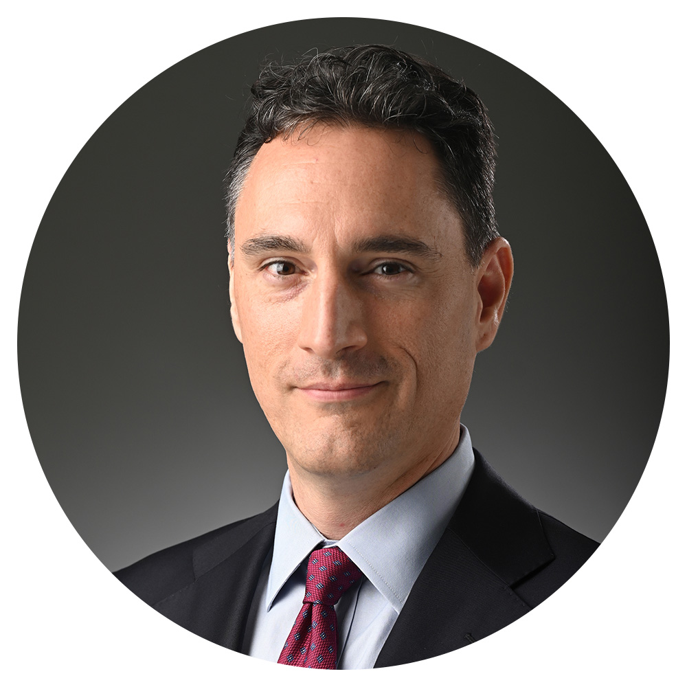 A man wearing a black suit, blue shirt, and red tie.