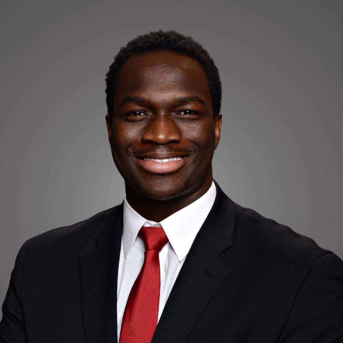 A man wearing a black suit with red tie.