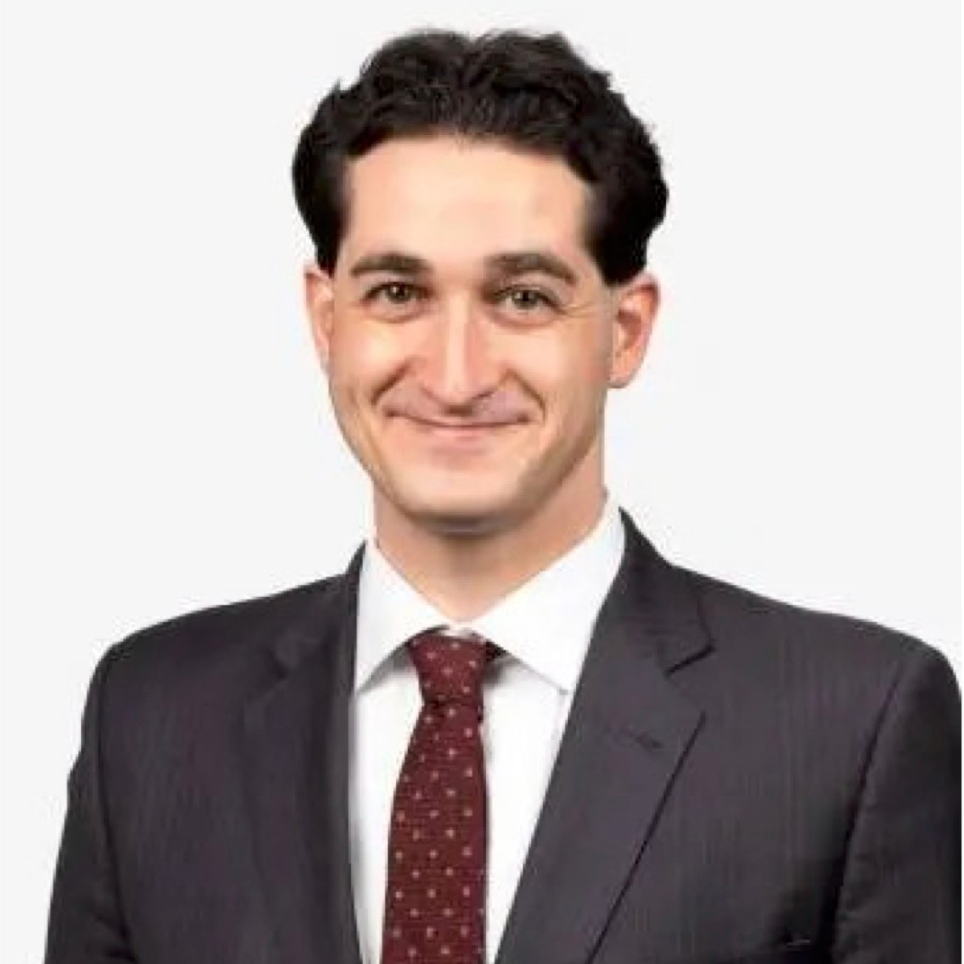 A man wearing a dark suit with a maroon patterned tie.