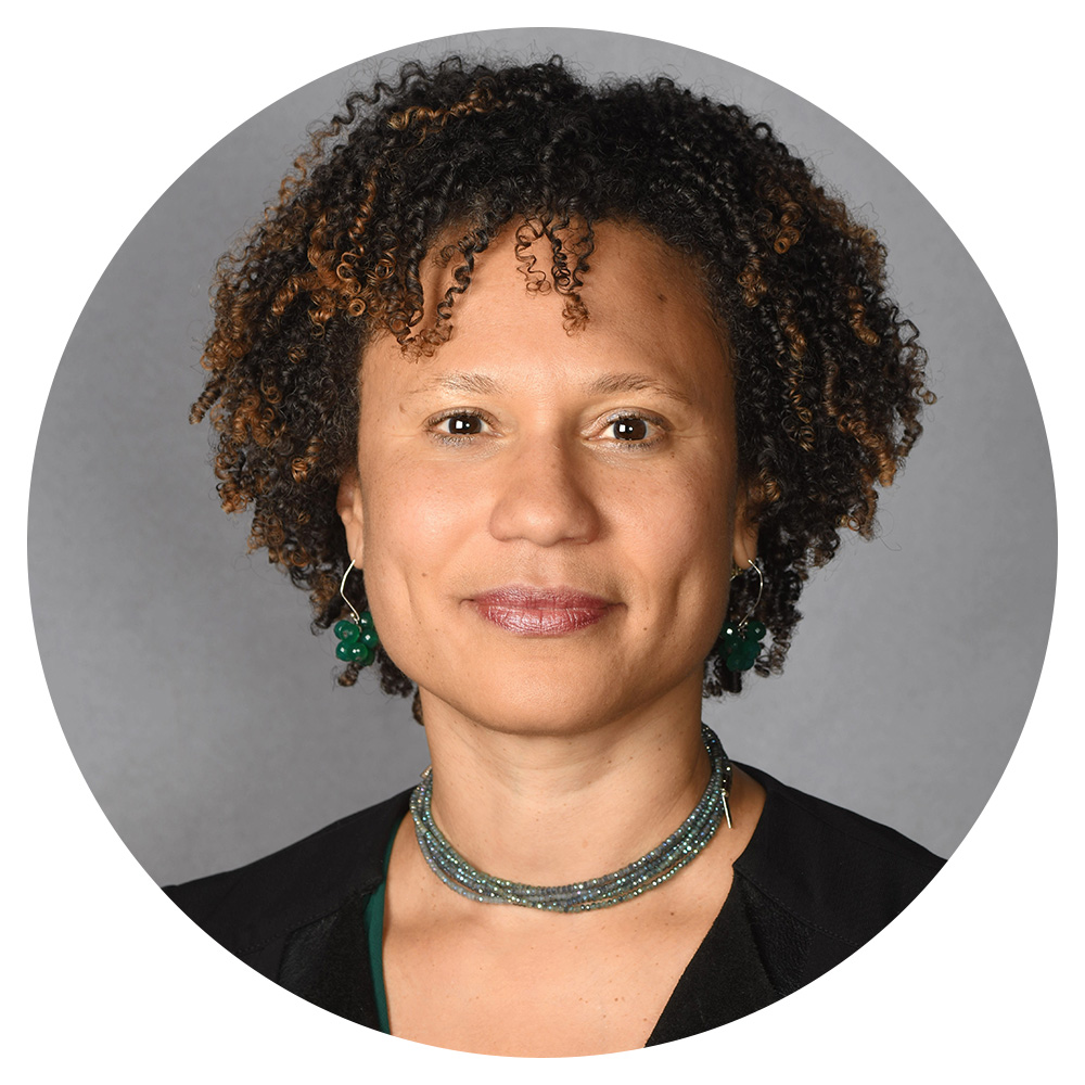 A woman with curly hair wearing a black blazer with green jewelry.