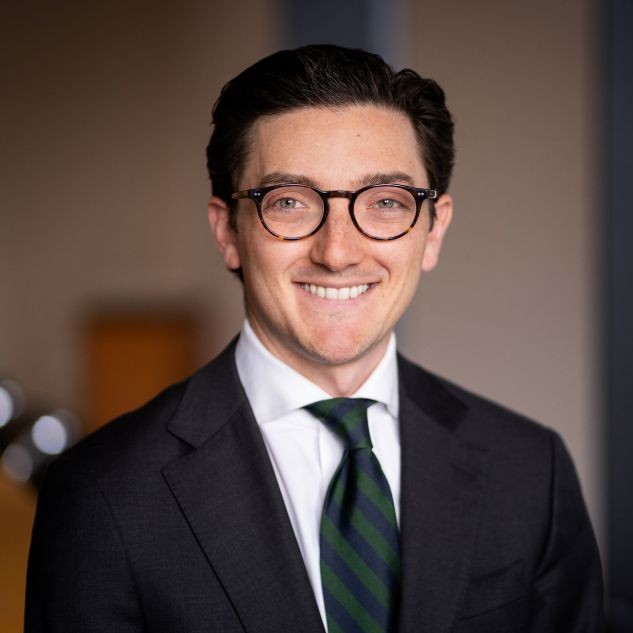 A man wearing a dark suit with glasses and a green striped tie.