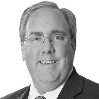 A man wearing a black suit and tie and eye glasses.