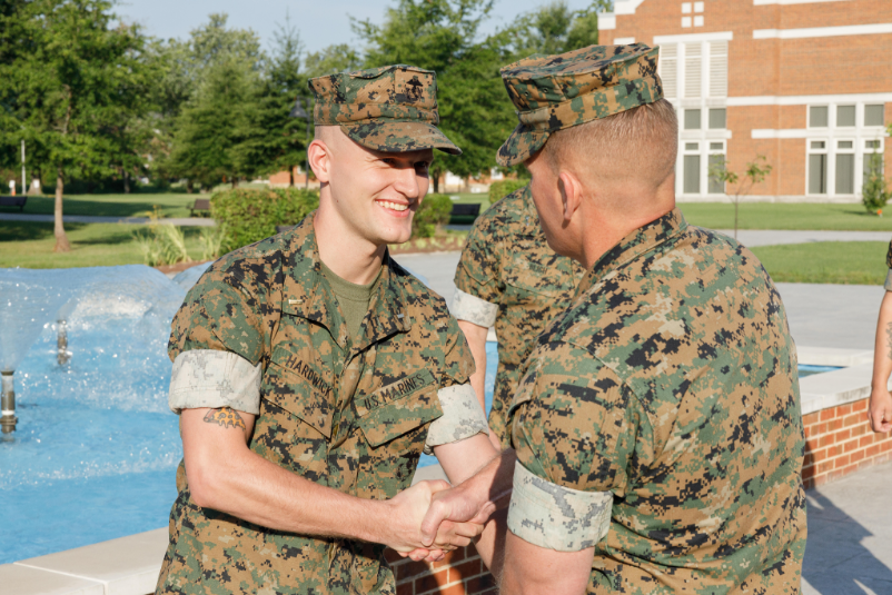Two men in camouflage army unifroms shaking hands.