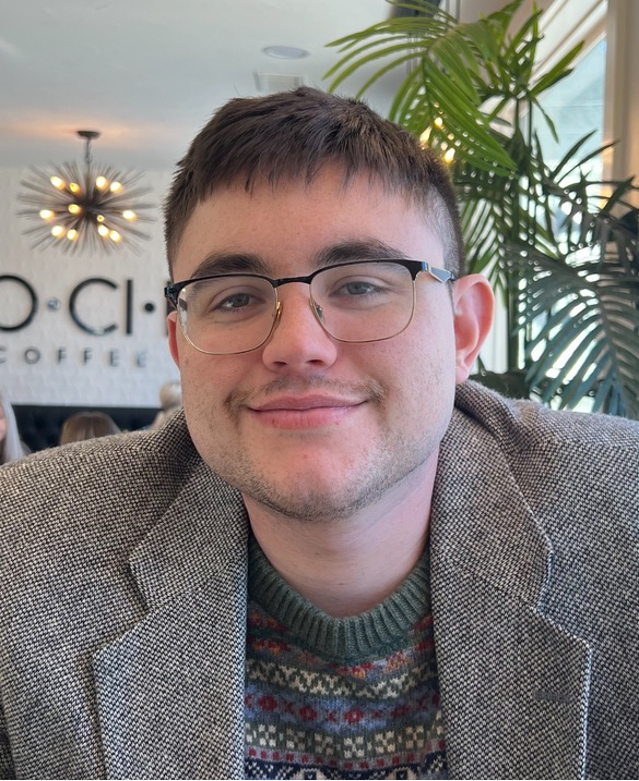 A man in a patterned suit wearing glasses inside a coffee shop.