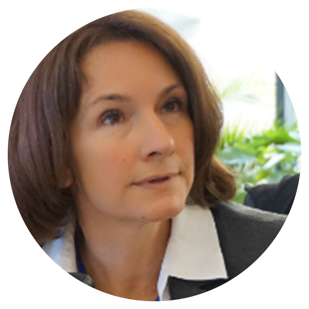 A woman with shoulder length hair wearing a white shirt and gray blazer.