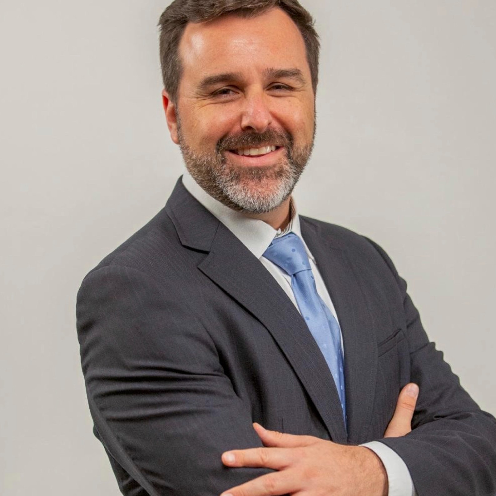 A man wearing a gray suit with a blue tie with his arms crossed.