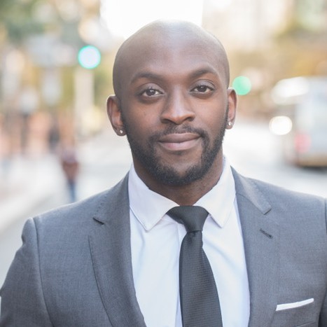 A man wearing a gray suit standing in front of the street.