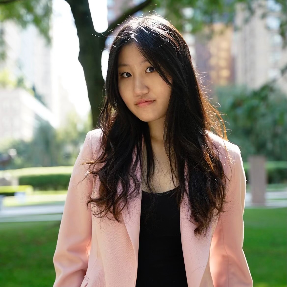 A woman with long dark hair wearing a black shirt and pink blazer.