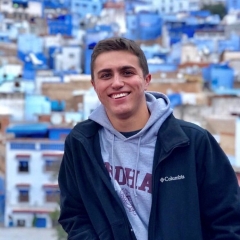 Student stands in front of white houses with blue roofs 