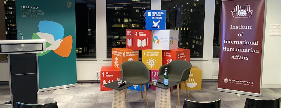 Room setup of chairs with a podium, two banners, and two sets of chairs in front of a display of the United Nations Sustainable Development Goals 