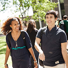 Two students smiling and walking on campus on summer day
