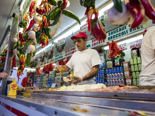Deli owner making a sandwich and peppers hanging above the grill